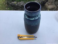 Full view of antique German pottery vase with dark brown and blue glaze placed next to a utility knife for size reference.