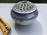 Top view of glazed porcelain bowl with ceramic flower frog lid, floral painted design in yellow and purple with metal rim