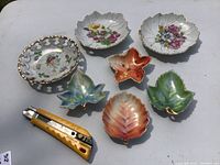 Top view of seven porcelain dishes including three floral bowls and four leaf-shaped dishes with vibrant colors and gold trim.