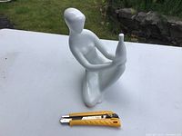 Side angle showing the full figure and reflective white glazed surface resting on white display surface outdoors.