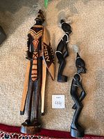 Set of three African wooden statues, two in black with feathers and one taller with intricate brown and black patterns.