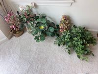 Full view of the artificial plants arranged on carpet showing pink floral stems, leafy plants, fruit clusters, and trailing greenery.