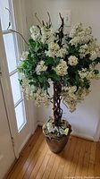 Full view of the artificial tree showing white hydrangea clusters, green leaves, brown twisting branches, and brown pot base.