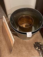 Three metal buckets stacked nested together with two wooden cutting boards leaning against them. Buckets vary in size and material; larger galvanized steel bucket and smaller hammered brass or copper buckets inside. Shows used condition with some surface marks.