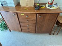 Front view of wooden sideboard buffet showing two cabinet doors on sides and five drawers in center with decorative metal knobs.