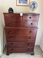 Front view of a tall wooden chest of drawers with round knobs, decorative moldings, and a smooth polished finish.
