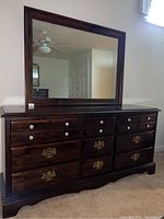 Front view of dark wood dresser with large mirror, showing drawer handles and knobs.