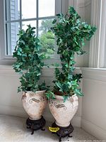 Full view of two potted fake ivy plants placed on wooden stands by window showing overall shape and size