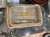 Overhead view showing three clear glass rectangular baking dishes nested inside matching woven wicker trays of corresponding sizes.