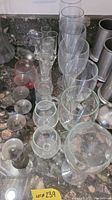 Photo showing multiple wine glasses and shot glasses of various sizes and designs on a dark countertop.