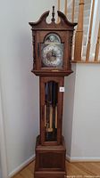 Full view of wooden grandfather clock showing arched bonnet, case, and lower base.