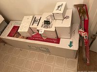 Boxes of Heritage Village Collection figurines and village pieces on top of a large box and miscellaneous holiday stakes/decorations boxed vertically.