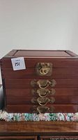 Front view of the wooden jewelry box showing four drawers with brass or copper handles and a top latch.