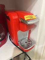 Red Keurig single-serve coffee maker front angle showing pod compartment and drip tray.