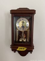 Front view of mini grandfather clock showing wooden case, clock face with Roman numerals, and pendulum beneath.