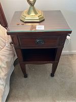 Front view of the wooden nightstand showing glass top, drawer, and shelf below.