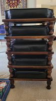 Stack of 5 ottomans showing wooden bases with turned legs and stacked black cushions.