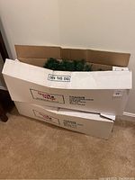Two stacked boxes labeled 'Good Tidings 3' Pre-Lit Norway Spruce Dark Green Multi Lights Made in Thailand' containing the trees.