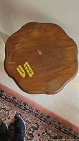Top view of wooden side table showing scalloped edges and surface wear with sticker on top.