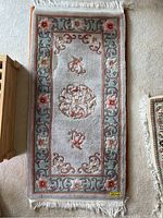 Full length of the small rectangular purple rug with floral design and white fringes on either end.