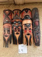 Front view of four small wooden tribal masks, showing detailed carvings and painted accents in red, black, and natural wood color.