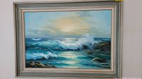 Full view of the framed ocean painting showing crashing waves and rocky coast under cloudy sky.