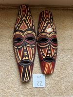 Two wooden tribal masks side by side showing front painted and carved details with geometric patterns primarily in black and red on natural wood.
