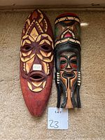 Two wooden tribal masks with detailed, carved facial designs and painted elements.