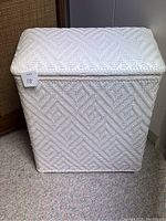 Front view of white woven laundry hamper showing textured pattern and intact lid.