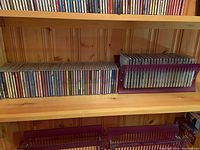 Wooden shelf with two rows of CDs and purple CD rack on left side.