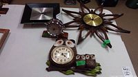 Four clocks displayed on a table: owl-themed Syroco clock with owlets front, small round clock with chrome frame, dark brown sunburst Airguide clock with gold face, and square Westclox clock with black frame and silver face.