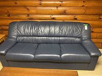 Full front view of dark blue leather couch showing three seating cushions, padded armrests, and a solid base.