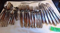 Cutlery including forks, knives, soup spoons, tea spoons laid out on a towel.