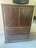 Front view of the complete wood dresser showing two doors with decorative carving and two drawers below with metal handles.