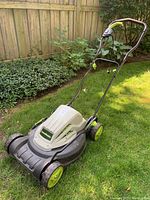 Electric lawnmower placed on grass showing side and front with green wheels and lawnmaster logo on the body.