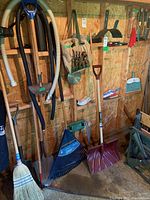 Full view of wall-mounted garden tools including shovels, rakes, broom, hand tool organizer, and snow shovel on shed wall