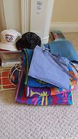 White and black hats in a plastic bin, towels and heating pad nearby, colorful carry bag on floor