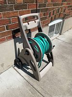 Side view of beige plastic hose reel with green garden hose coiled. Shows handle, wheels, and crank.