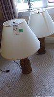 Pair of table lamps with white shades on carpet near window