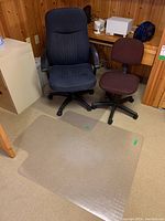 Two office chairs and one plastic chair mat on the floor in wood-paneled room corner, showing approximate sizes and condition