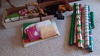Photo of assorted office supplies, stationery, envelopes, Christmas wrapping paper rolls, and cardboard boxes on carpet