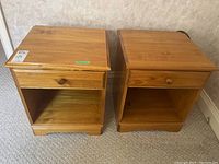 Two wooden side tables placed next to each other showing front view with one drawer and open cubby below.
