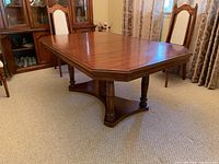 View of rectangular wooden dining table with polished wood surface and extension leaf attached, showing turned legs and base stretcher.