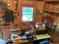 Wide view of workbench with various boxed tools, Shark vacuum cleaner, hand tools, and hardware supplies on and around table.