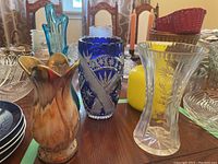 Set of five vases showing different materials and styles including ceramic, crystal, and glass on a table.