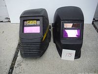 Front view of two black welding helmets with purple viewing windows and yellow Eye-Tech marking on one helmet.