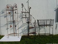 Three large metal plant stands set against an outdoor wall, showing full height and form of each stand.
