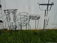 All four metal plant stands arranged outdoors opposite a white wall on grass, showing varying heights and styles