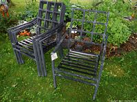 Four black lightweight aluminum patio chairs grouped on grass with garden background, showing overall condition and design.