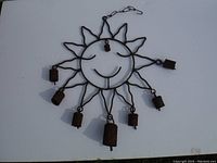 Full view of a metal sun wall art with seven bells hanging from the rays and one bell in the center, showing the entire shape and size.